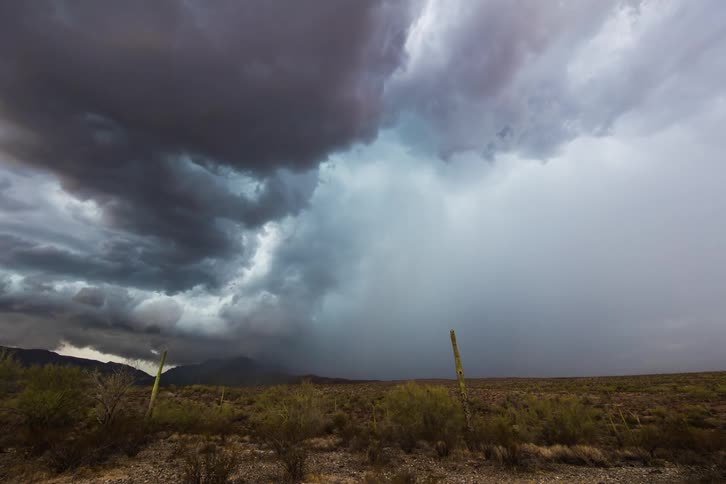Dark storm clouds forming over a field and distant mountains in nature