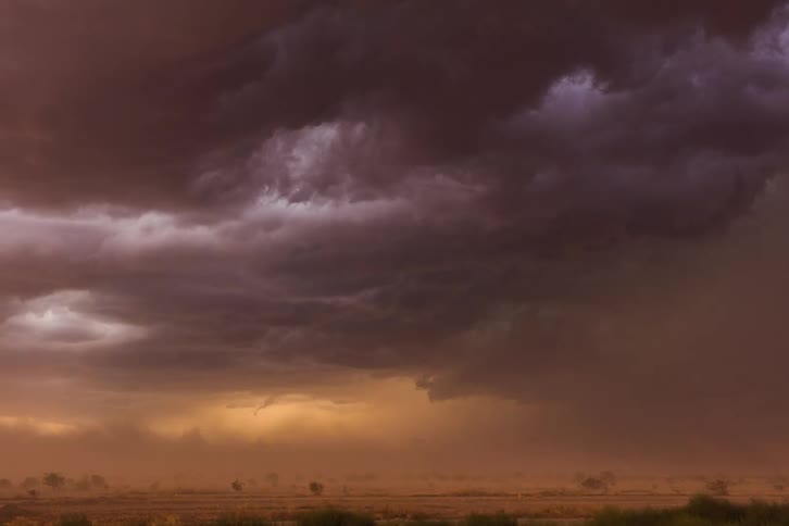 Dark storm clouds and blowing dust flowsacross deserts and mountains obscuring terrain