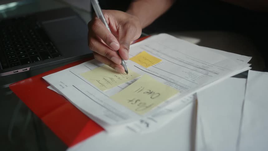 Cu hand holding a pen and writing on a postit note stuck to a past due bill on a desk