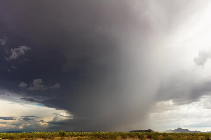 Lightning strikes though storm downburst moving across plains near mountains