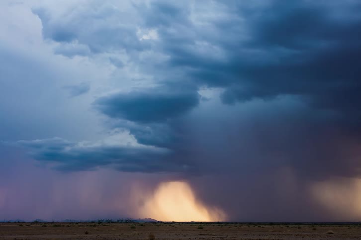 Dark storm clouds and strong downbursts are moving over rural land as lightning flashes