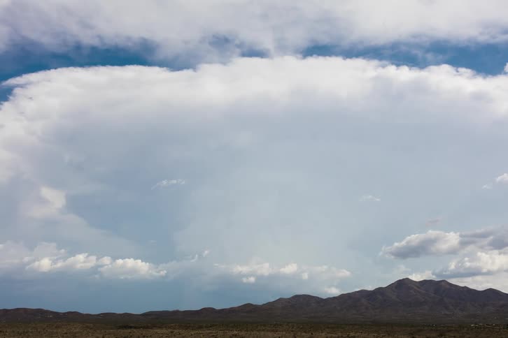 Clouds slowly fill the sky over a mountain ridge in a grassland during the day