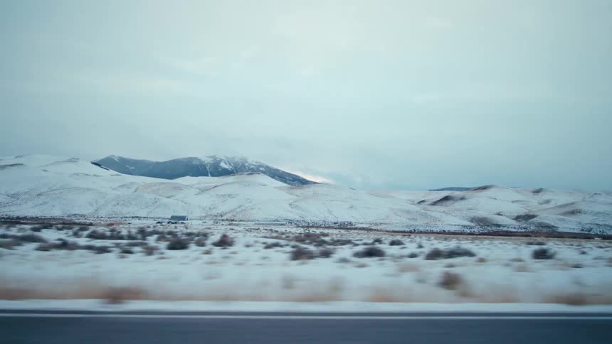 Another vehicle going the opposite direction mountains and the pastures near a farm are passed during a winter road trip