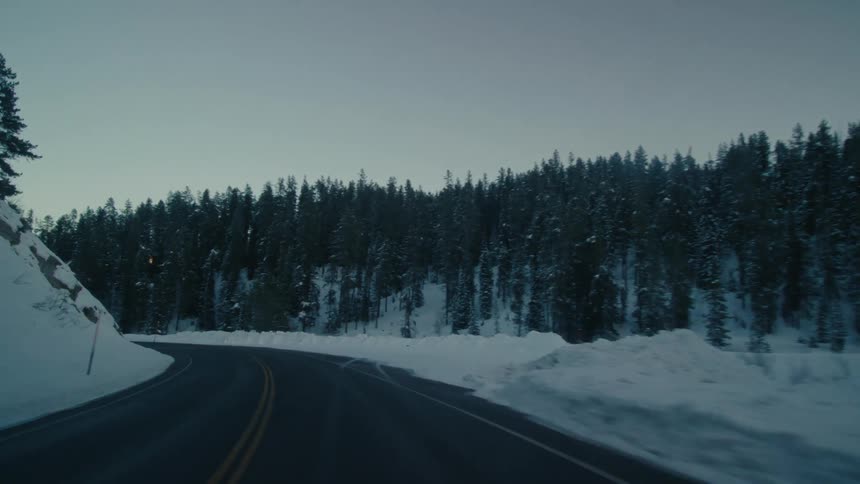 Vehicle drives on highway near snowy forest at dusk