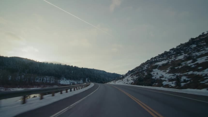 A highway runs past a forest covered with a dusting of snow