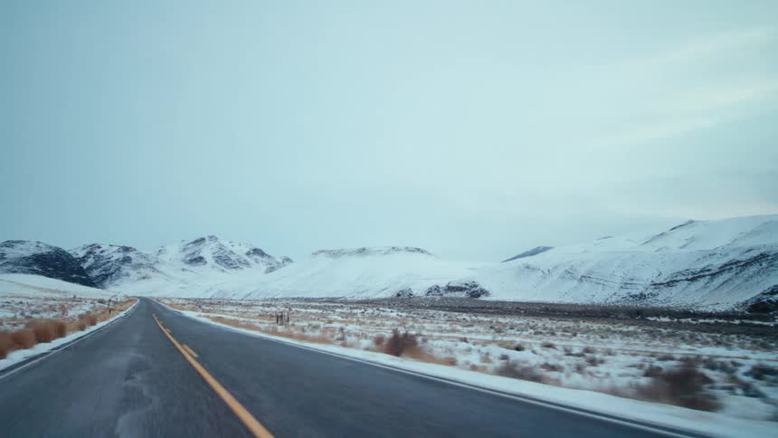 Pov from rear window of car traveling on twolane highway along snowy landscape with snowy mountains in background