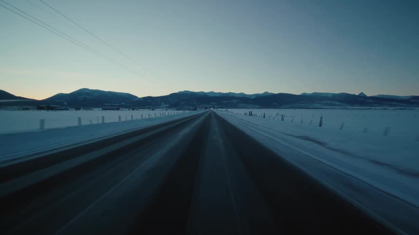 Moving on a rural road with snow covering the ground and mountains in the distance under a clear sky