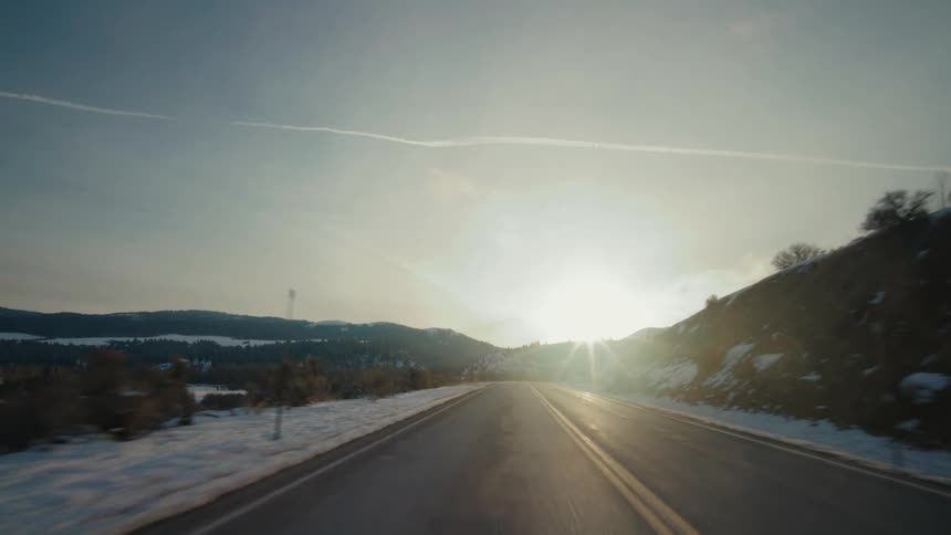 Vehicle drives on highway near the snowy field at sunset
