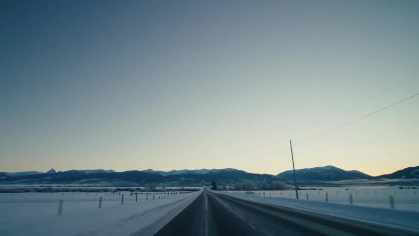 Moving on a rural road with snow covering the ground and mountains in the distance under a clear sky