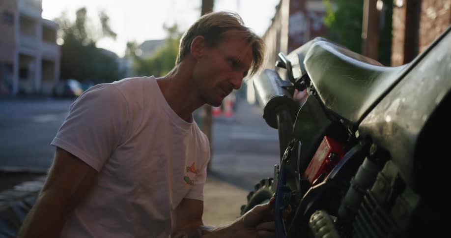 A man takes a side panel off of a motorcycle and inspects what is under it