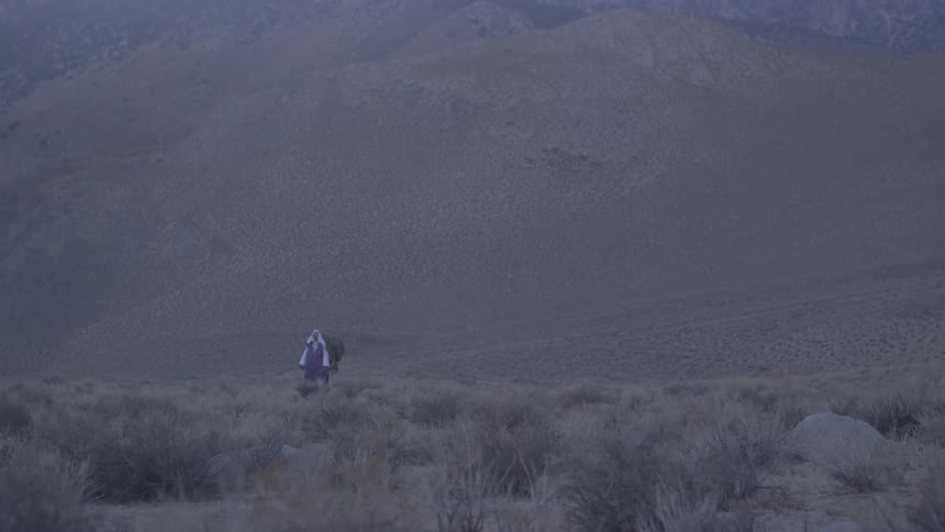 A man leading his horse across a prairie at the foot of the mountains