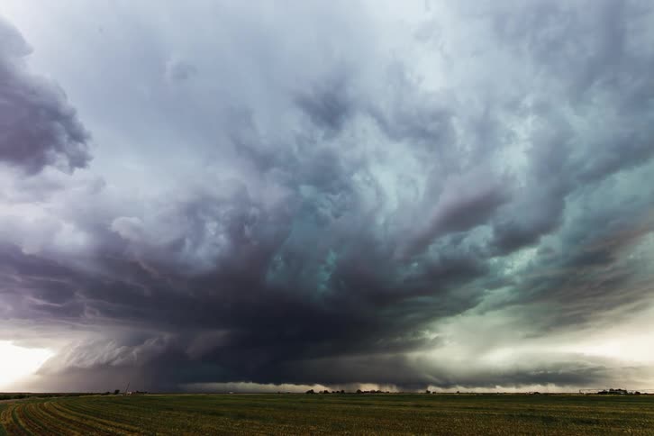 Traffic flows along country road as dark storm clouds tint green and start rotating