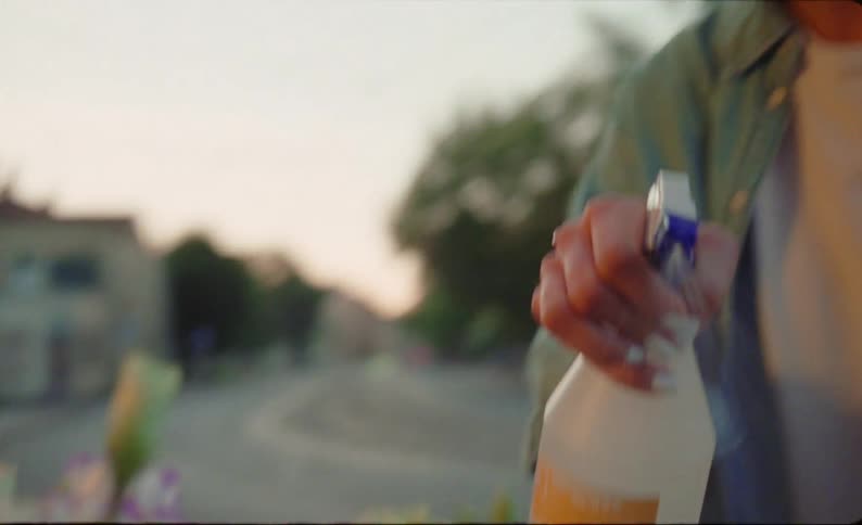 Woman with denim shirt and white top sprays water on bunch of flowers in front of flower store at dusk in the street