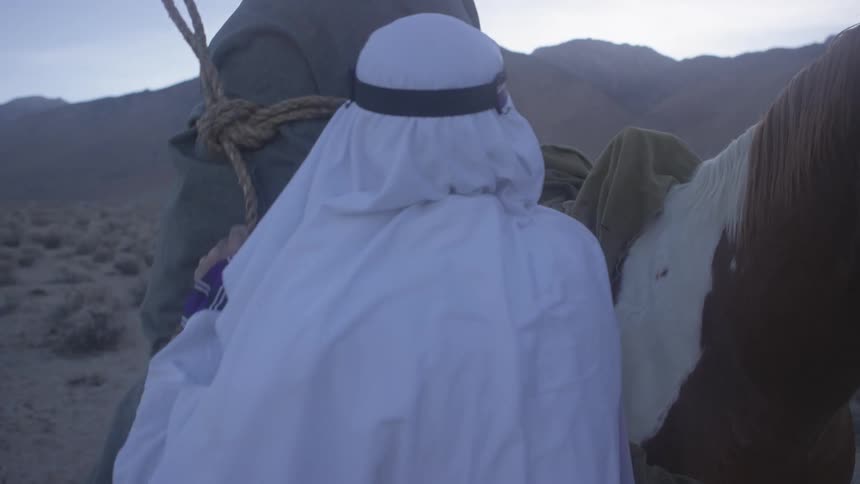 A male wearing middle eastern style clothing loads a bundle on a horse