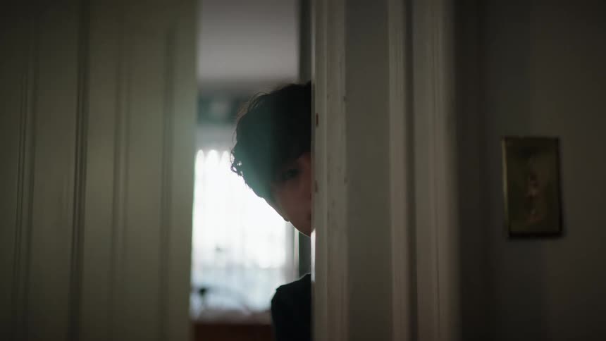 A boy slowly peeks around a doorway in house during the day