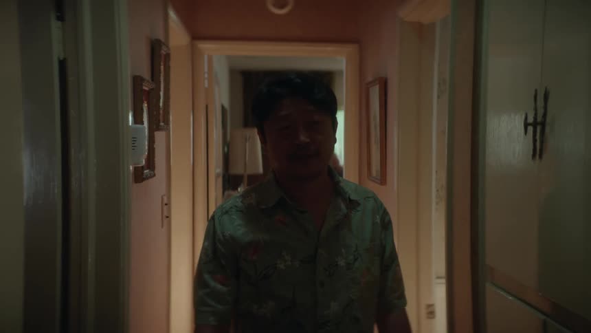 Man with blue shirt walks along dark hallway at house