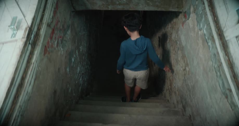 A young boy is walking down a dark stairway leading under a building
