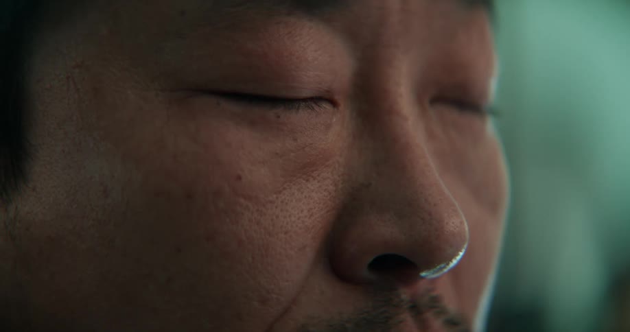 A man crying with his eyes closed and wiping away a tear