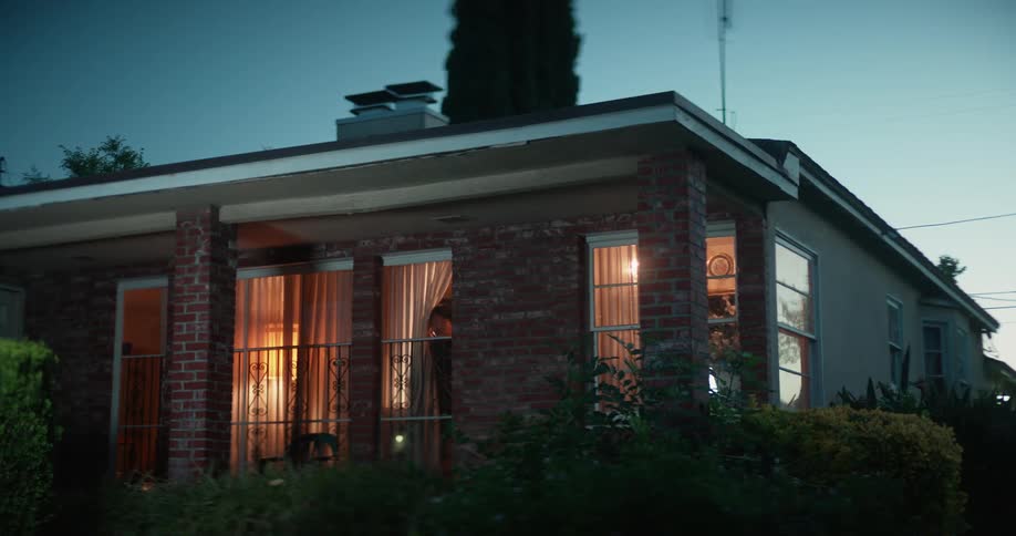 Exterior of home a person pulls back drapes and peers out the window