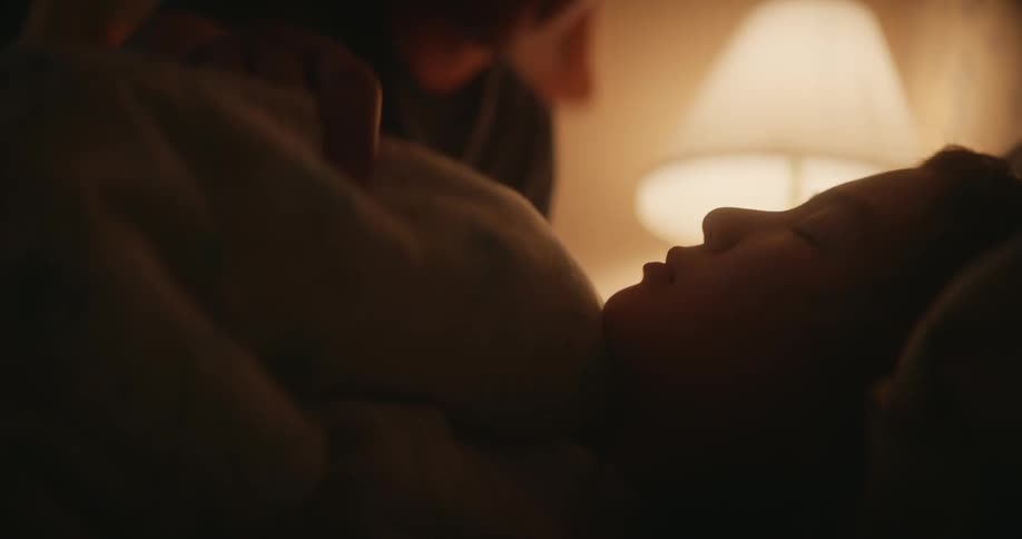 Father kisses daughters forehead and puts blanket on her in her room