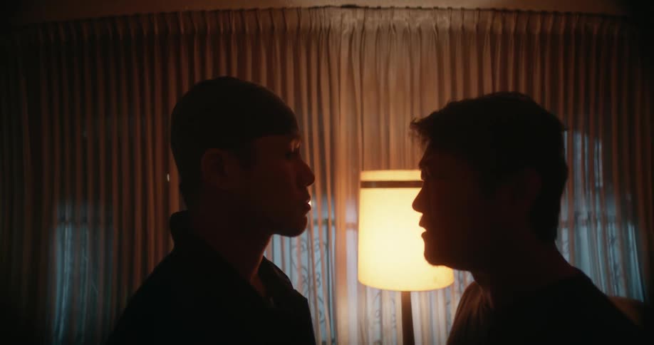 Two men stand facing each other in a home their faces showing strong emotion