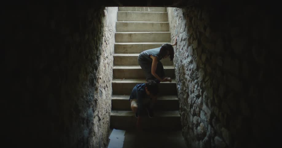 A boy is playing on the bottom stair of a staircase and his mother climbs down the stairs takes him by the hand and they both climb the stairs