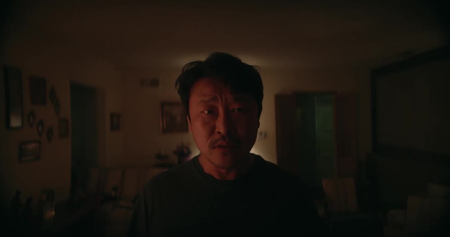 Man stares forward while muttering as he stands in a dimly lit room