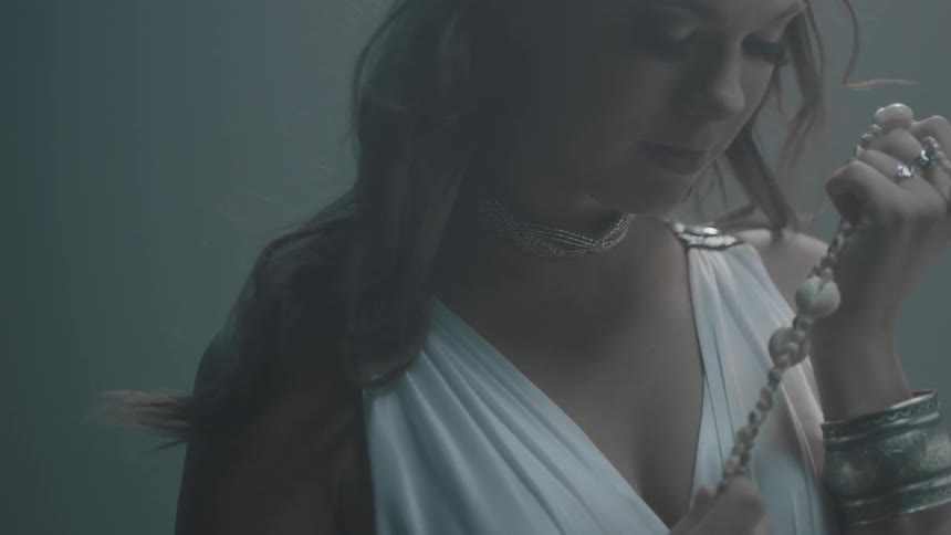Long-haired woman in a gown embracing her necklace