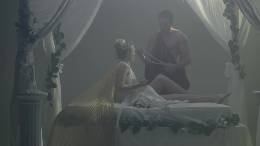 A roman man approaching a woman resting on a canopy bed and handing her an object