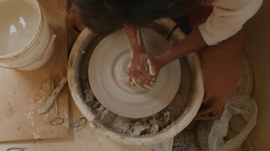 A craftsperson uses the pottery wheel to make pots out of clay