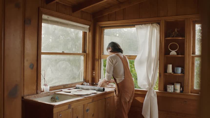 A woman stands at a counter aggressively rolling dough with a rolling pin