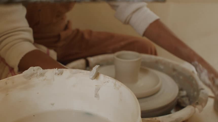 A woman spins clay on a pottery wheel
