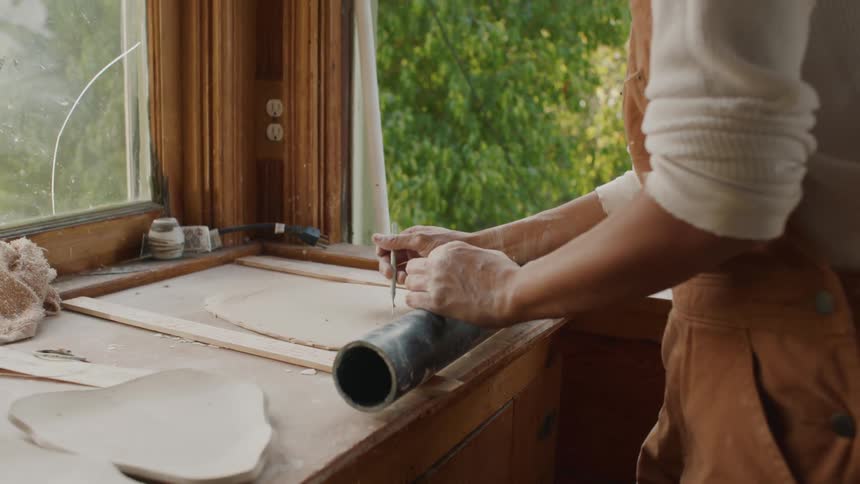A woman pricks holes on a piece of pottery that she rolled out