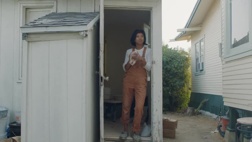 A woman wipes her hands while standing in the doorway of her shed