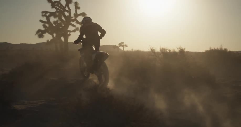A person riding a dirt bike through the desert at dusk