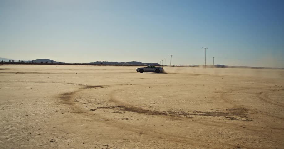 A car drives in circles in a flat sandy area by utility poles