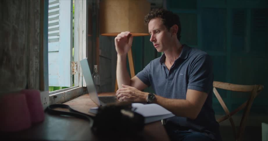 A man flips through the pages of a book before beginning to type on a laptop