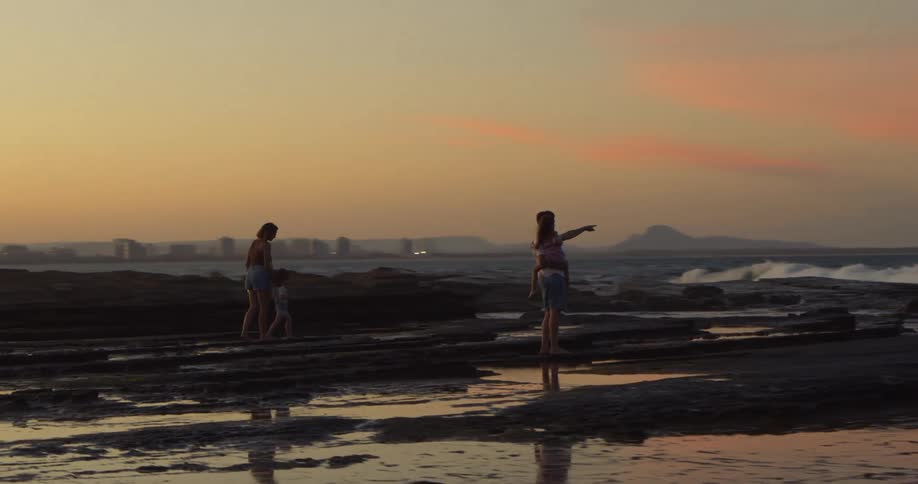 Family with two daughters moves along beach under red tinted sky
