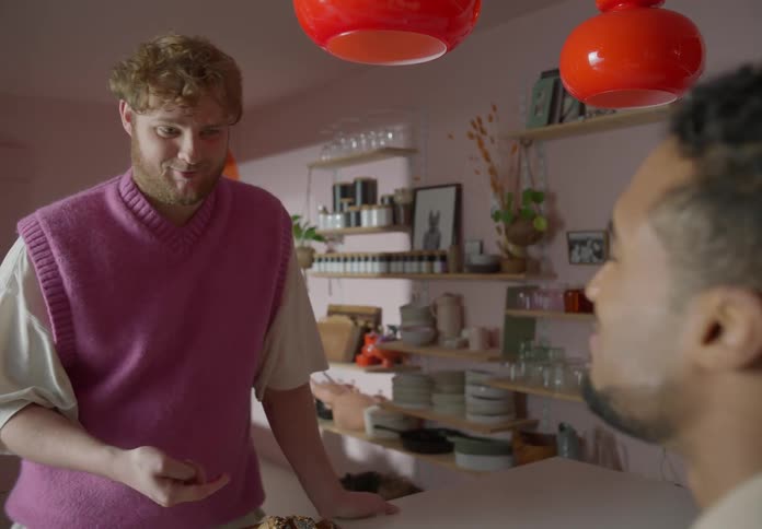 A man swipes jelly off another mans toast with his finger in a kitchen