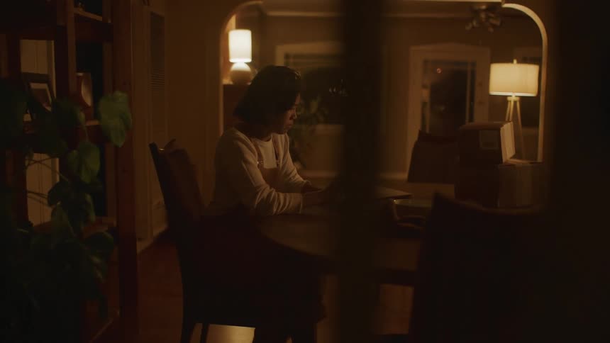 Woman sits at table at home at night using smartphone
