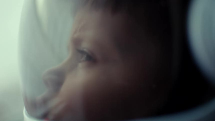 A young boy is wearing an astronaut helmet as he looks ahead