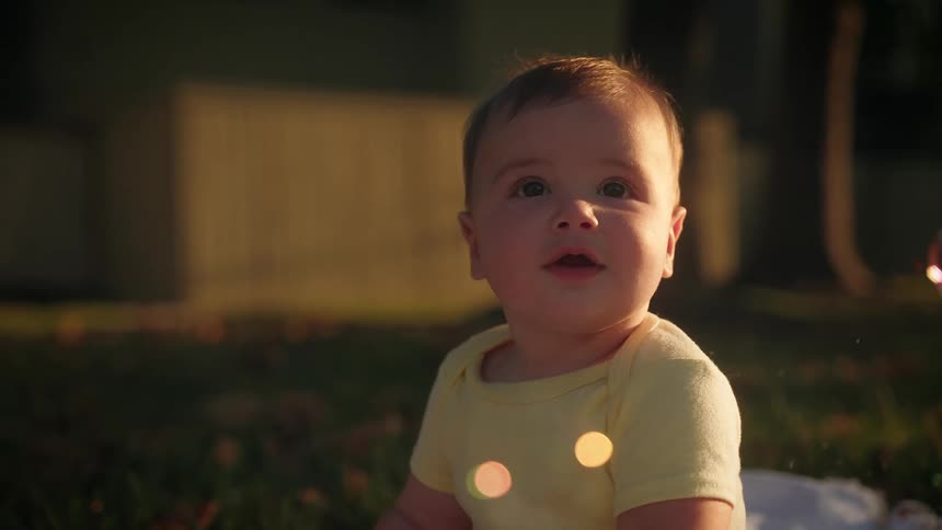 Baby sitting on blanket in yard watches falling bubbles
