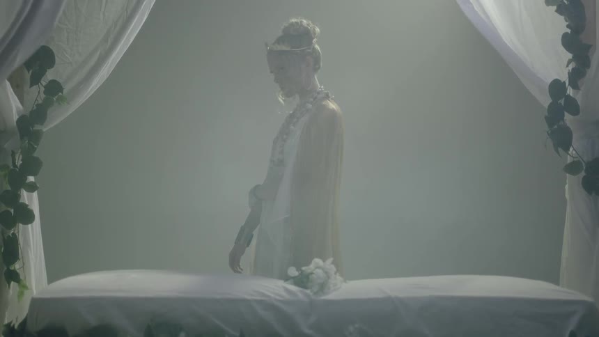 Goddess dressed woman standing next to a bed