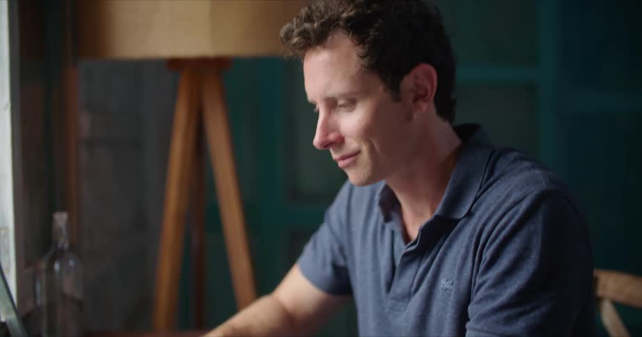 Man with blue shirt works on laptop smiling