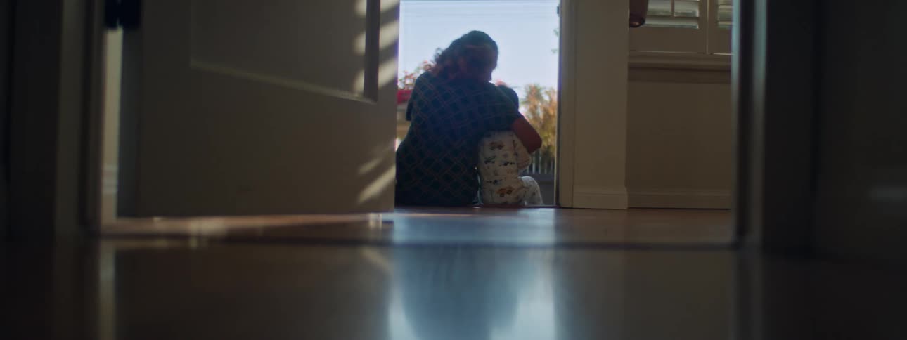 A woman is sitting on the front steps of her house with her arm around her little boy as he stands up