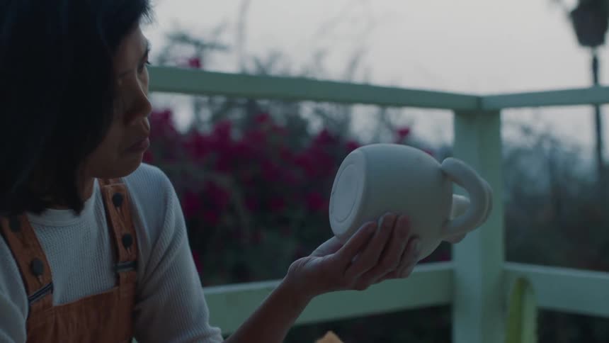 A woman uses a towel to polish the bottom of a newly made teapot