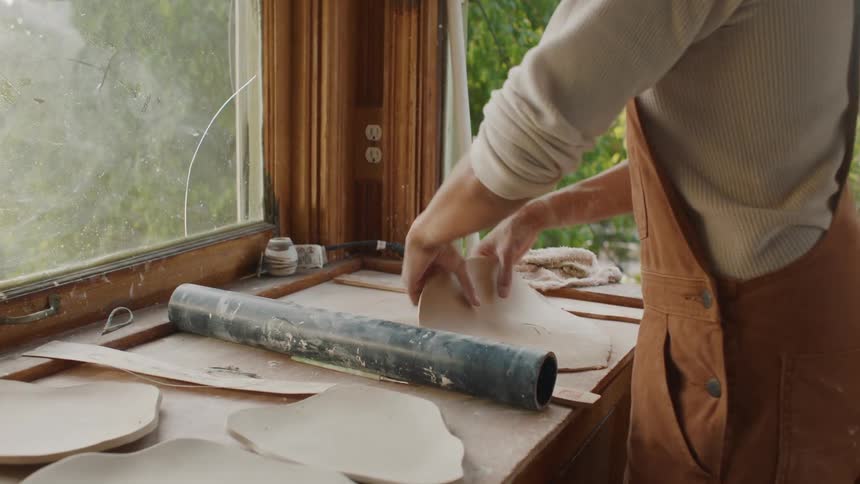 A woman is standing in a kitchen flipping flat dough on a cutting board