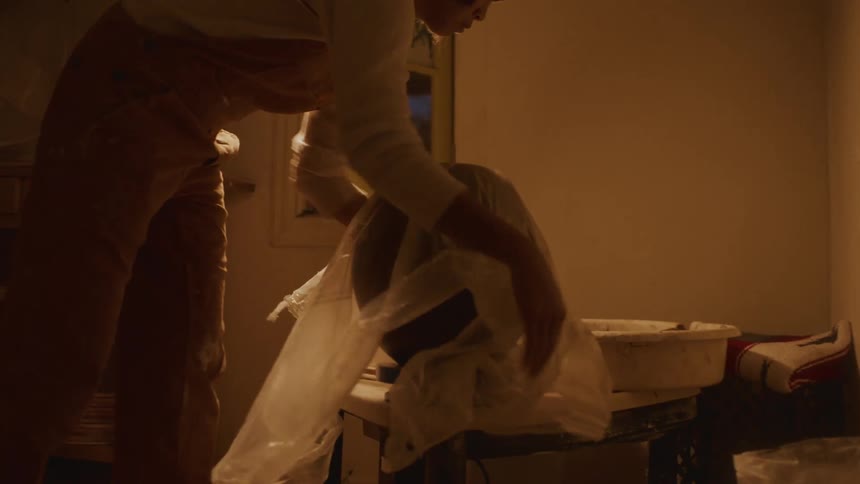 A woman at home covers up pottery with a plastic sheet