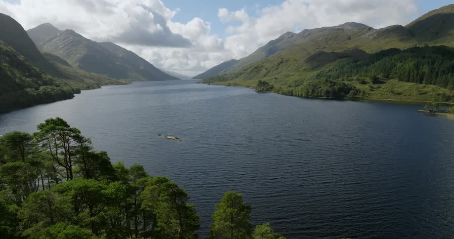 An aerial view of a lake surrounded by hills flying over trees