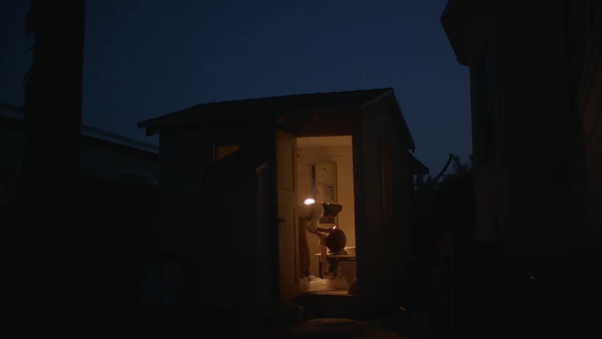 Woman works in clay in shed at night